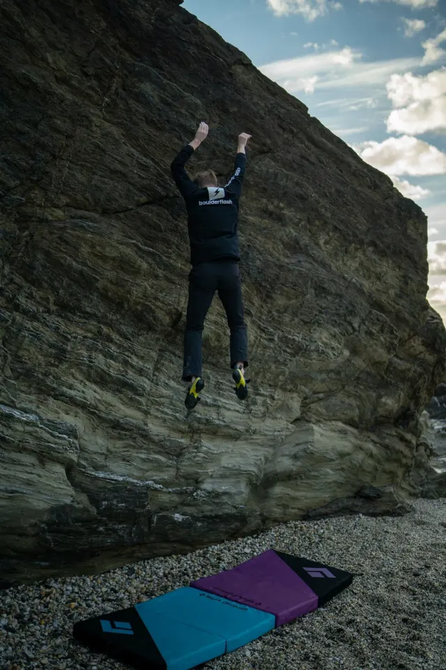 Spotter positioning a crash pad under an outdoor boulder problem